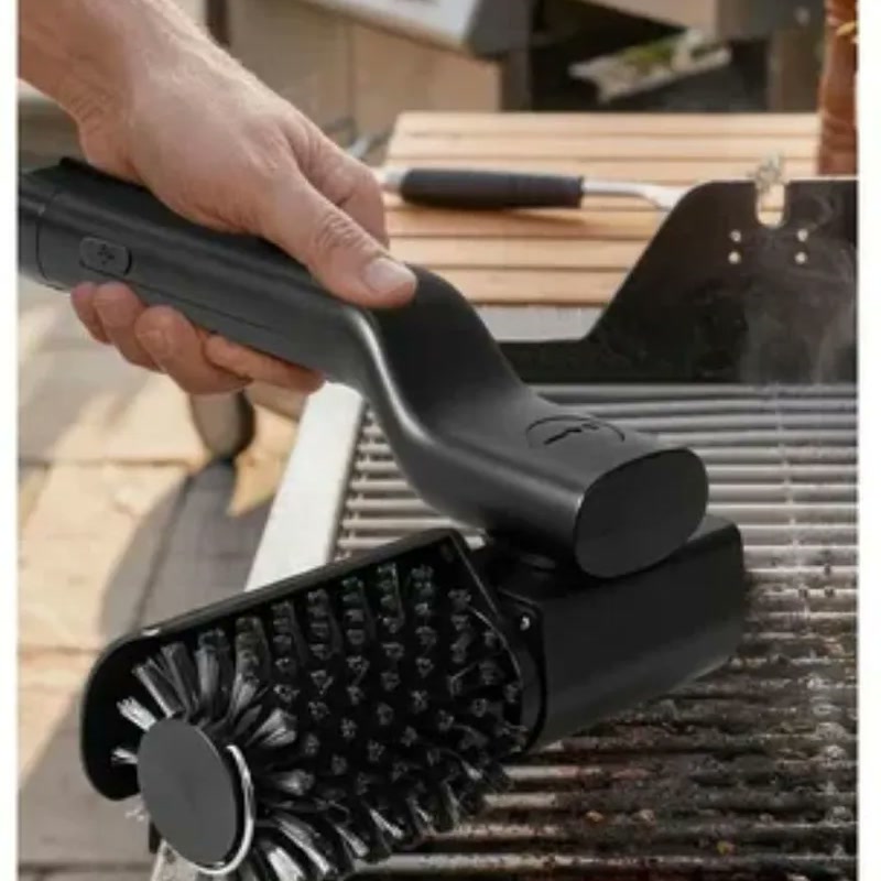 Mano sosteniendo el cepillo eléctrico GRILLO sobre la rejilla de una parrilla