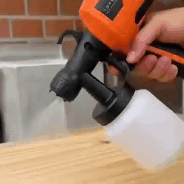 La pistola de pintura naranja rociando pintura sobre una tabla de madera