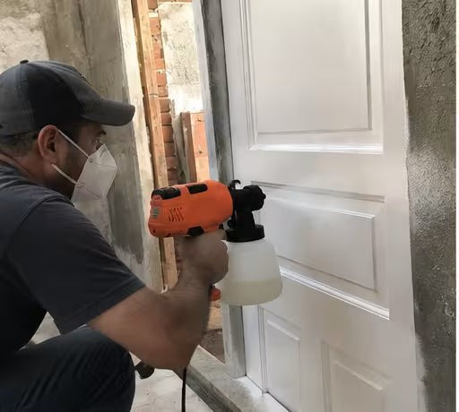 Hombre pintando una puerta blanca con la pistola de pintura
