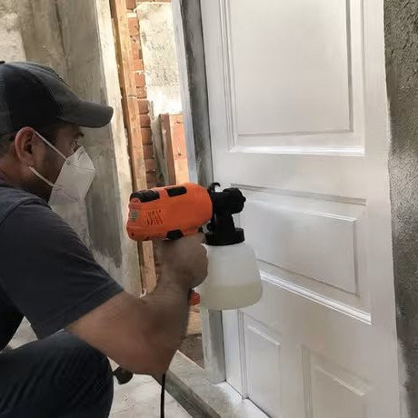 Hombre pintando una puerta blanca con la pistola de pintura
