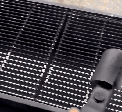 Cepillo eléctrico limpiando la rejilla de una parrilla de carbón